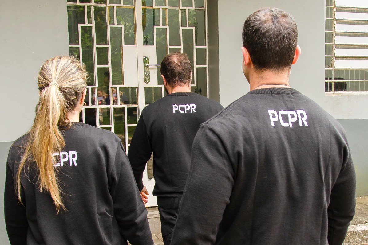 Três policiais civis de costas entrando em delegacia
