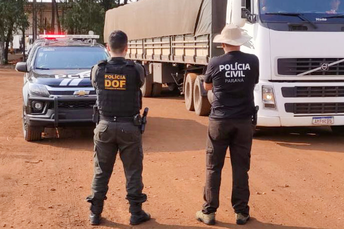 Dois policiais de costas observam caminhao com droga apreendida