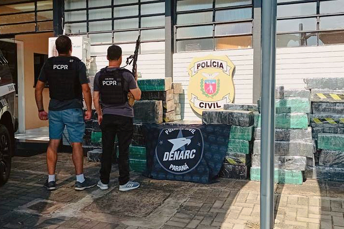 Dois policiais civis ao lado de pacotes com droga apreendida