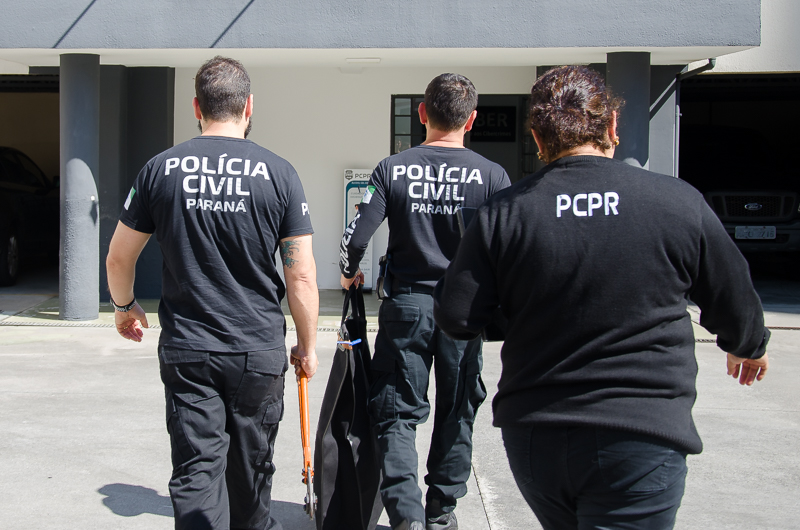 Três policiais civis de costas entrando em delegacia