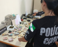 Policiais civis organizam, sobre uma mesa, drogas, armas, dinheiro e produtos apreendidos