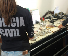 Policiais civis organizam, sobre uma mesa, drogas, armas, dinheiro e produtos apreendidos