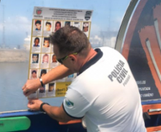 Policial da PCPR colando cartaz de crianças desaparecidas