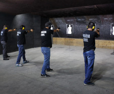 Policiais civis alinhados em pé, apontando suas armas para alvos de papel, no interior de um estande de tiro