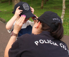 Policial civil agachada, colocando boné em criança