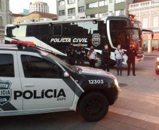 Policiais civis posando para foto entre viaturas e ônibus da PCPR