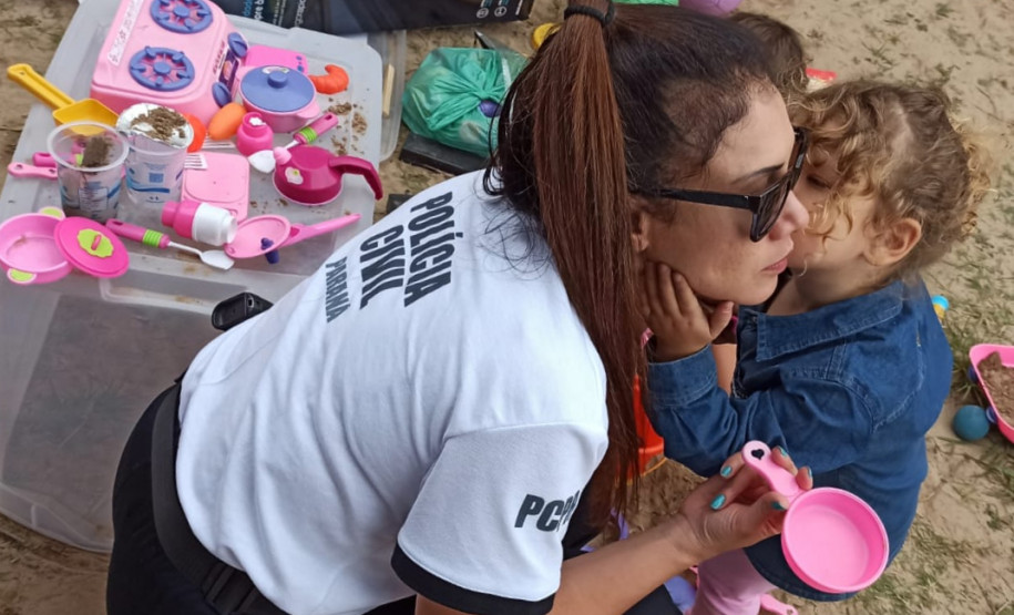 Criança dá um beijo no rosto de uma policial civil, em meio aos brinquedos