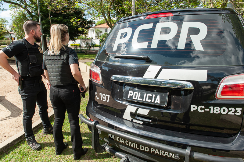 Dois policiais civis ao lado de viatura