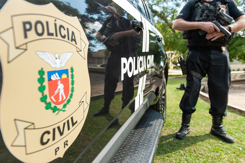 Policial civil empunhando arma ao lado de viatura