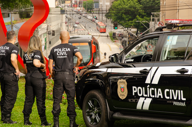 Três policiais civis ao lado de viatura