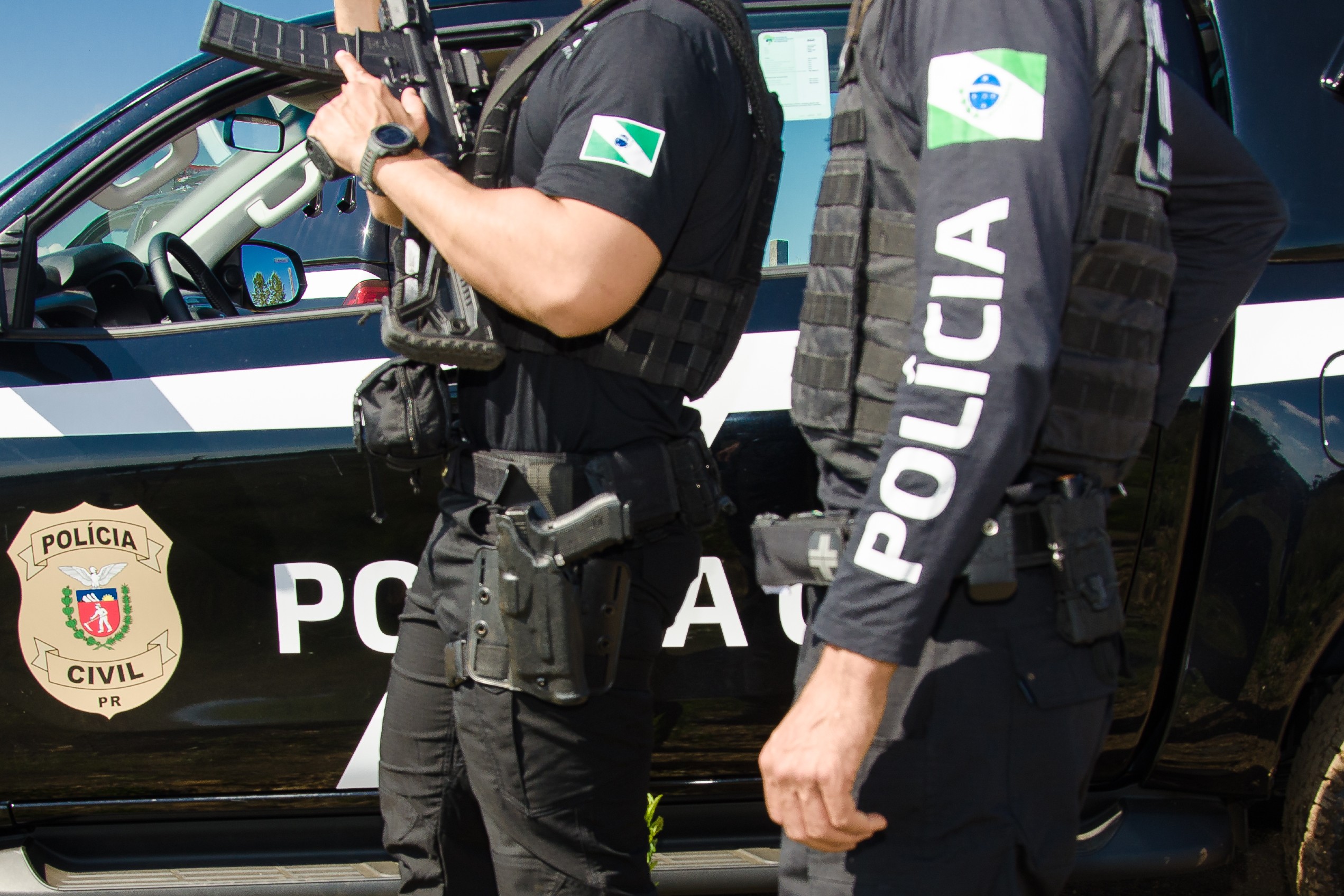 Dois policiais civis ao lado de viatura