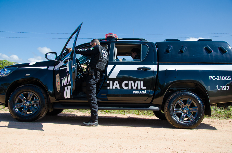 Policial civil apontando arma ao lado de viatura