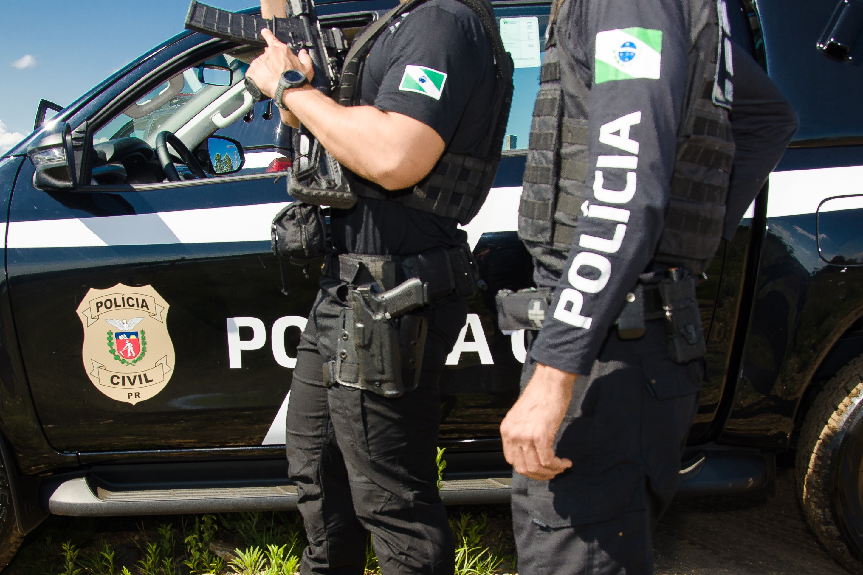 Dois policiais civis ao lado de viatura