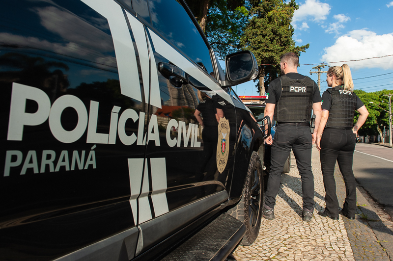 Dois policiais civis ao lado de viatura