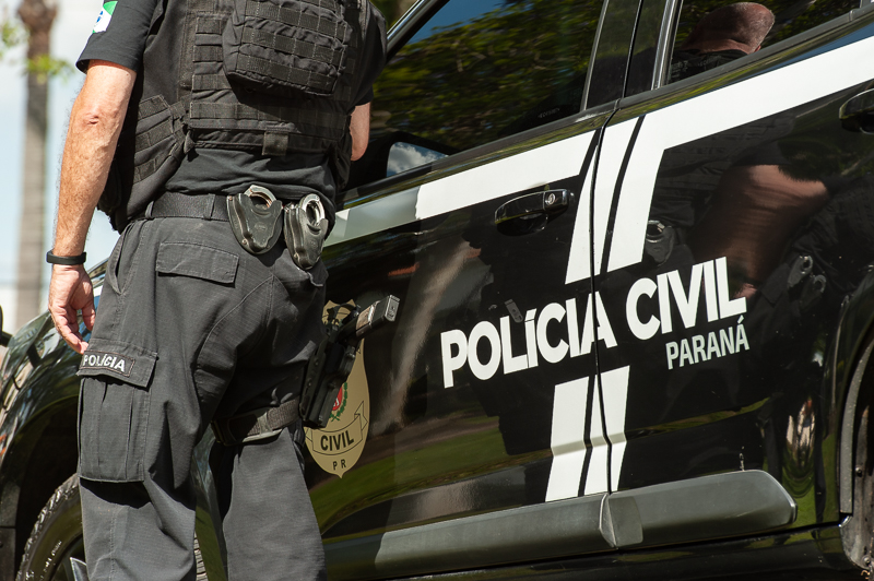 Policial civil de costas ao lado de viatura