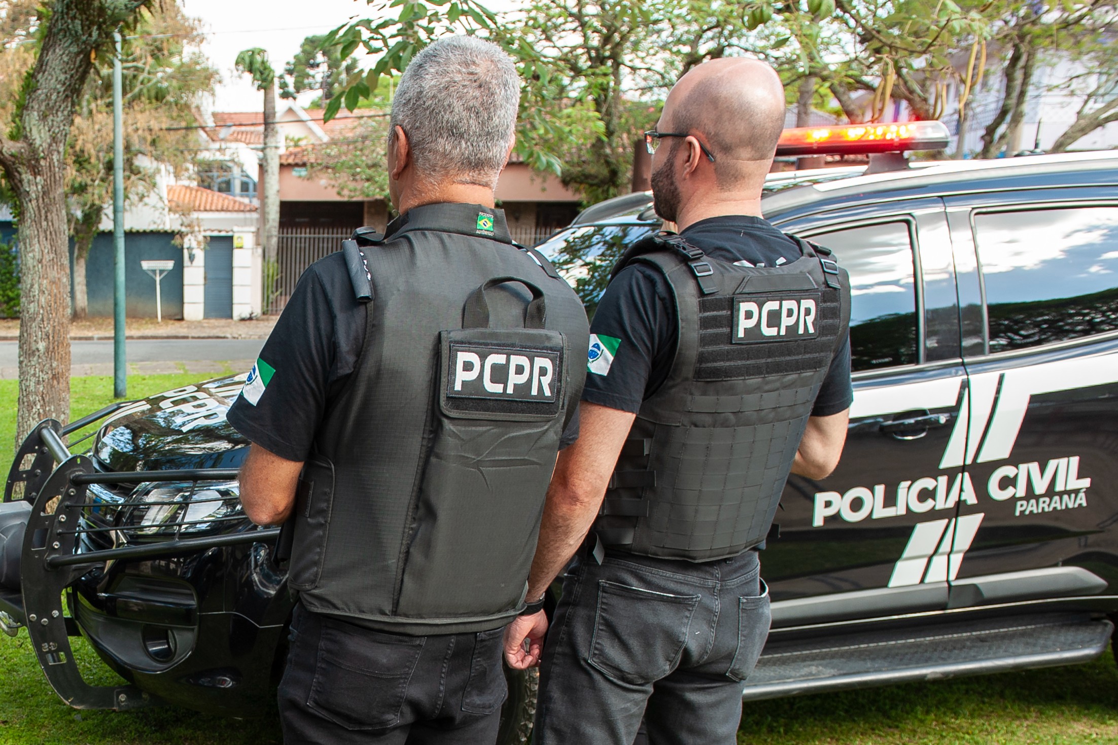 Dois policiais civis ao lado de viatura