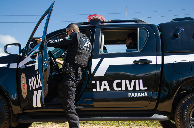 Policial civil ao lado de viatura apontando arma em abordagem