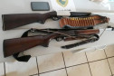 Duas armas, munição e um celular apreendidos, sobre uma mesa