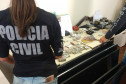 Policiais civis organizam, sobre uma mesa, drogas, armas, dinheiro e produtos apreendidos
