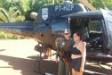 Mulher sendo fotografada ao lado de policial civil com helicóptero atrás