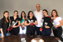 Seis mulheres segurando rosas vermelhas posando para foto junto ao delegado