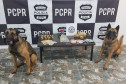Mesa com drogas e dinheiro apreendidos entre dois cães farejadores