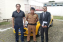 Participantes da reunião em pé, posando para foto. Ao fundo, viatura da polícia militar