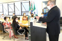 Participantes reunidos à mesa, enquanto uma pessoa, no púlpito, apresenta o material
