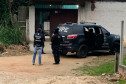 Policiais civis ao lado de viatura, em frente à uma residência