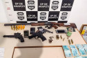 Material apreendido, sobre uma mesa. Ao fundo, banner da policia civil