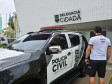 Policial civil ao lado de viatura, em frente à delegacia