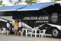 Duas policiais civis atendendo uma veranista ao lado do ônibus com a delegacia móvel