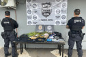 Dois policiais de costas ao lado de mesa com produtos apreendidos