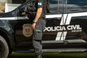 Policial civil ao ao lado de viatura