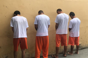 Quatro homens presos, voltados para a parede.