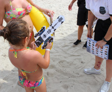 Policial civil distribuindo material preventivo na areia da praia para população