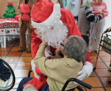 Senhora fazendo carinho em Papai Noel durante entrega de presente 