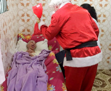 Papai Noel entregando presente para idosa acamada
