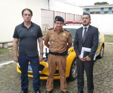 Participantes da reunião em pé, posando para foto. Ao fundo, viatura da polícia militar