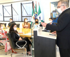 Participantes reunidos à mesa, enquanto uma pessoa, no púlpito, apresenta o material