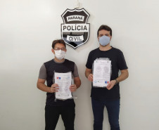 Policiais civis segurando embalagens com as máscaras. Ao fundo, brasão da Polícia Civil.