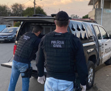 Dois policiais civis atrás de uma viatura com a tampa do porta-malas aberta
