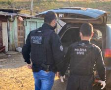 Dois policiais civis atrás de uma viatura com a tampa do porta-malas aberta