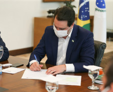 Governador sentado à mesa, assinando documento