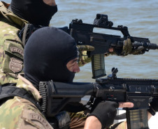 Dois policiais civis na proa do barco, apontando armas