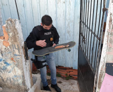 Policial saindo por portão de residência com skate e faca nas mãos