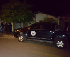 Policiais entrando um uma residência. Ao lado, viatura estacionada.