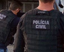 Dois policiais civis ao lado de viatura