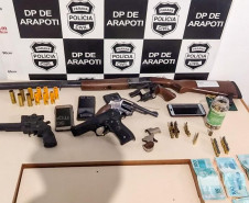 Material apreendido, sobre uma mesa. Ao fundo, banner da policia civil