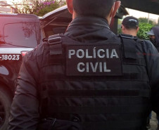 Policial civil de costas, próximo à viatura